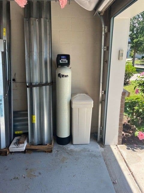Titan whole-home water treatment system and storage tank in a garage.