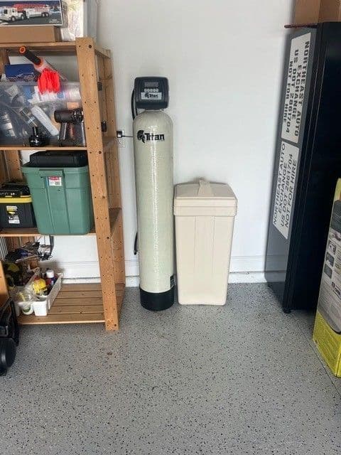 Titan whole-home water treatment system and salt tank in a garage next to a shelving unit.