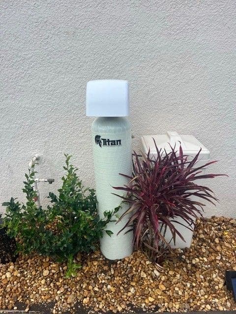 Water filtration system by a building, surrounded by plants and gravel.