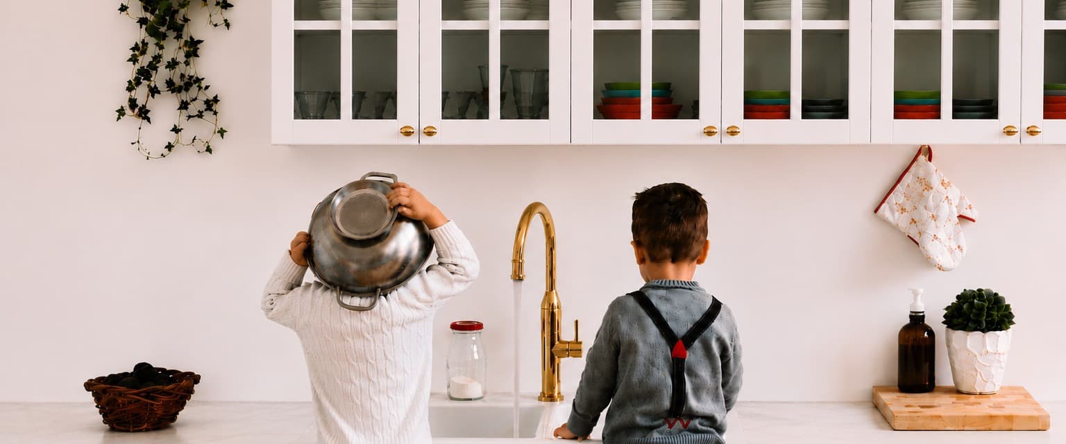 Two children playing at a kitchen sink with clean water
