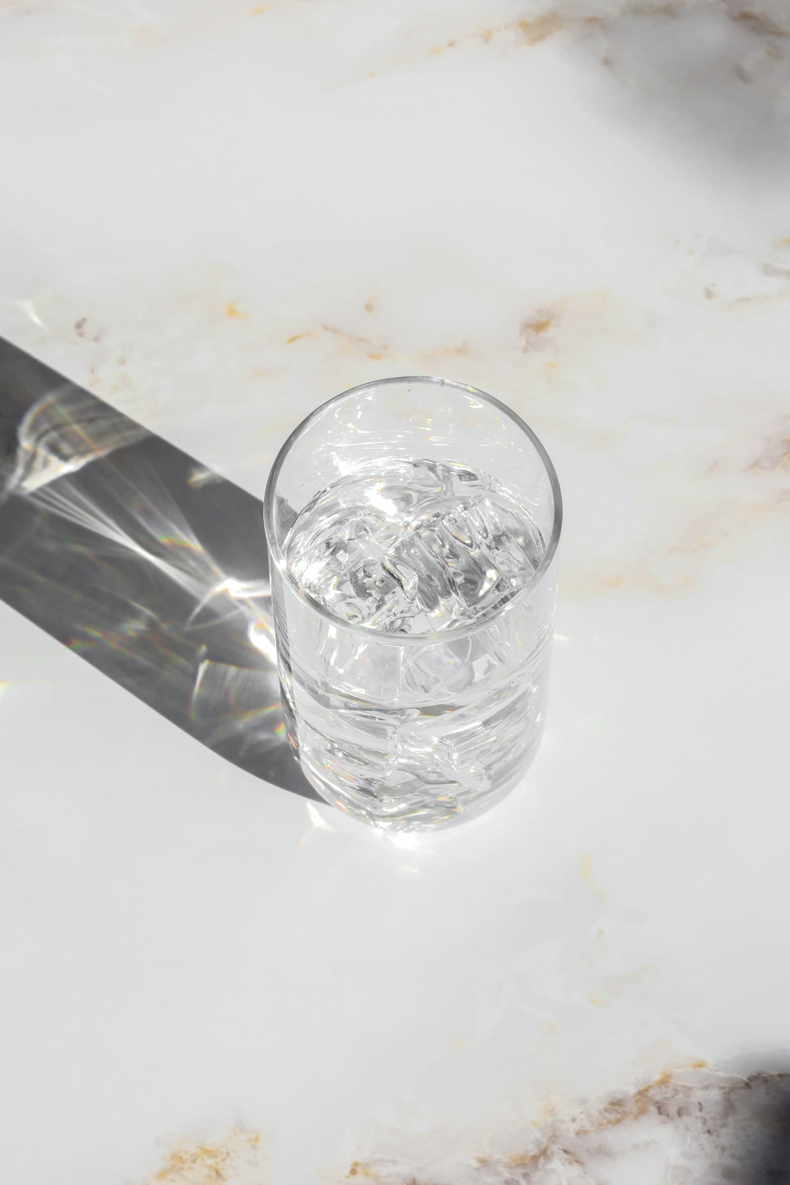 A clear glass of clean water catching sunlight on a bright marble counter